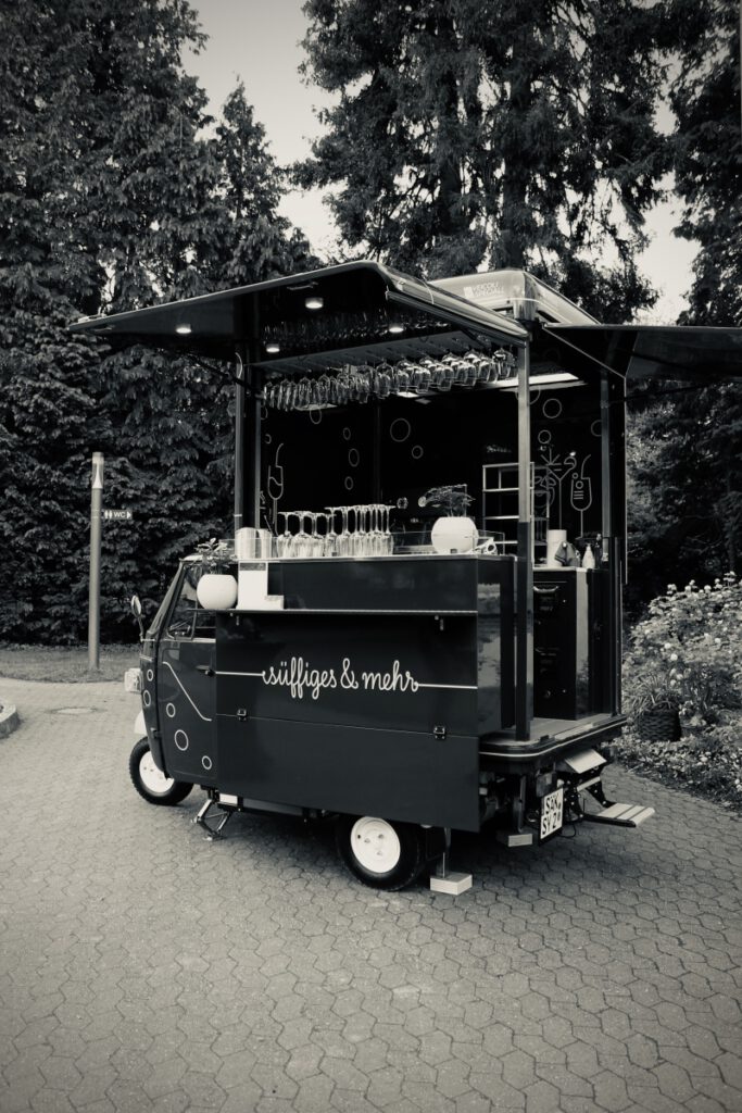 Das Zwuggele mit Gläserregal vor einer Hecke im Schlosspark